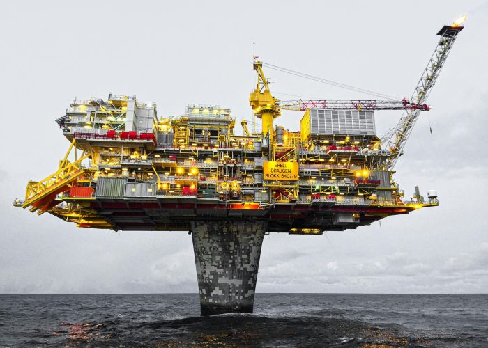 A well-lit offshore oil platform against a cloudy sky in Norway's waters.